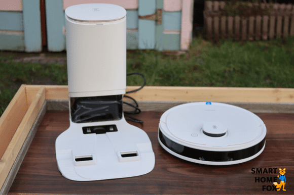 The Ecovacs Deebot N8+ stands on the floor beside the auto-empty dust bin.